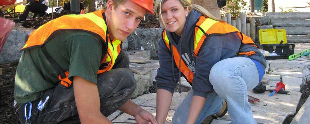Two students work to set paving stones